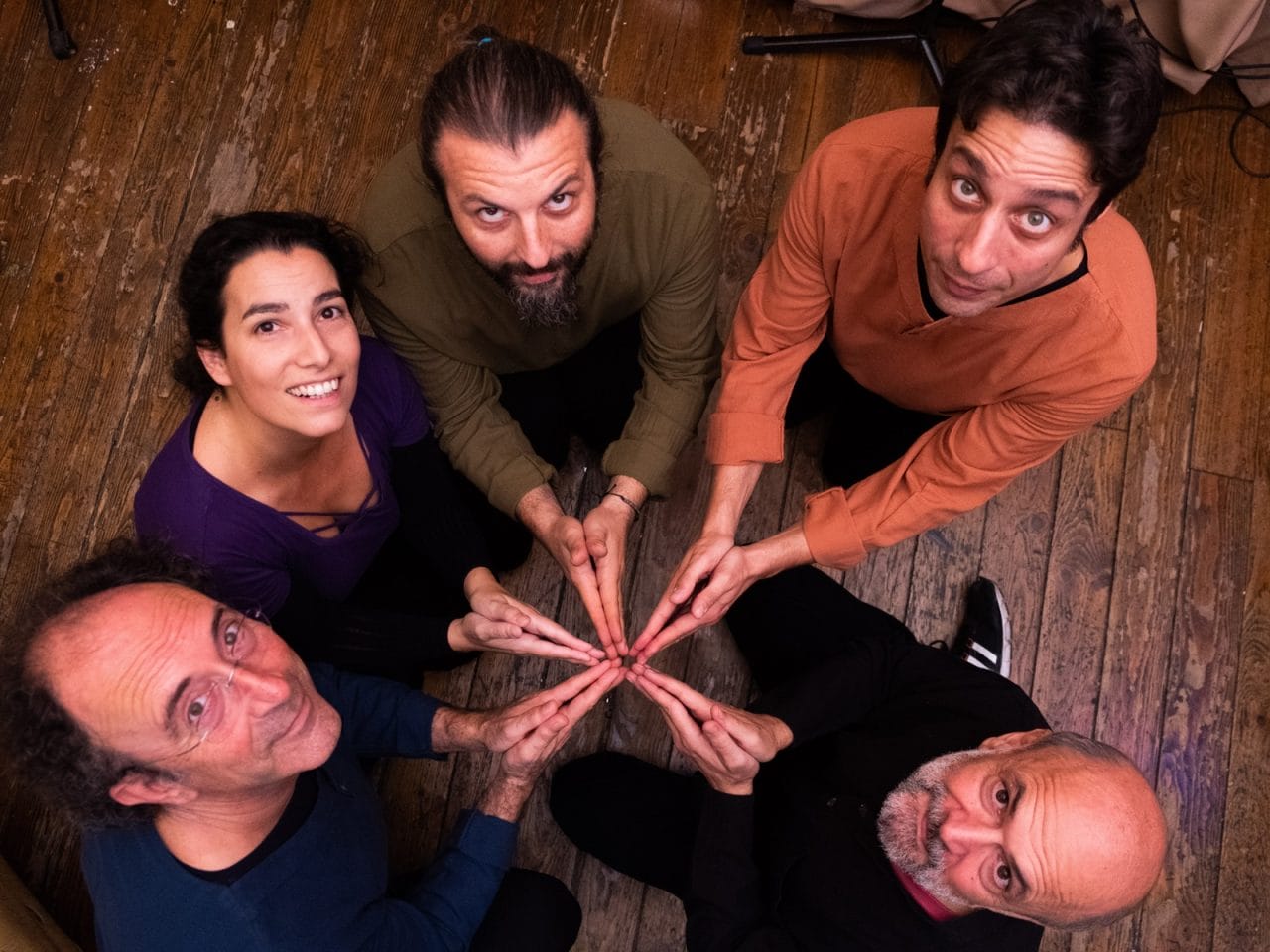 Five people looking up towards the camera smiling, they all have their hands in the middle making a star shape.