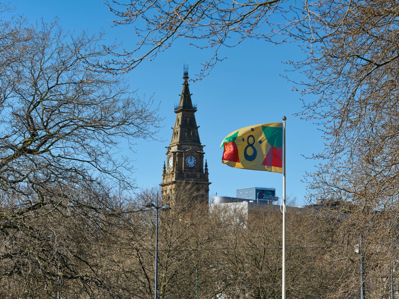 a yellow flag in the wind, it has a black 8 symbol in the centre and green and red shapes mirroring either side.