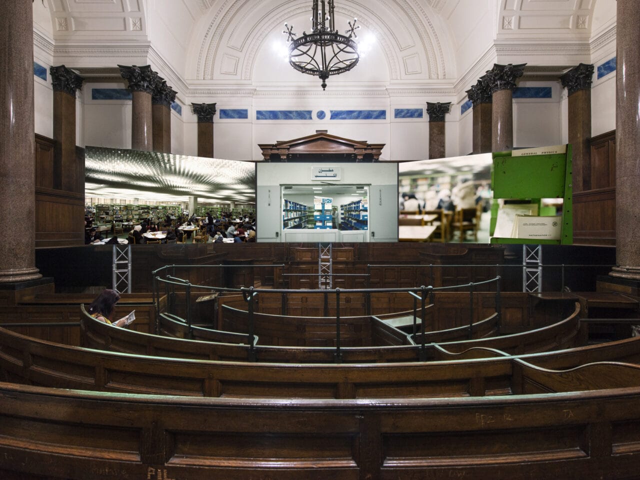 A courtroom with a three-channel film shown amongst a circular dark wooden seating area