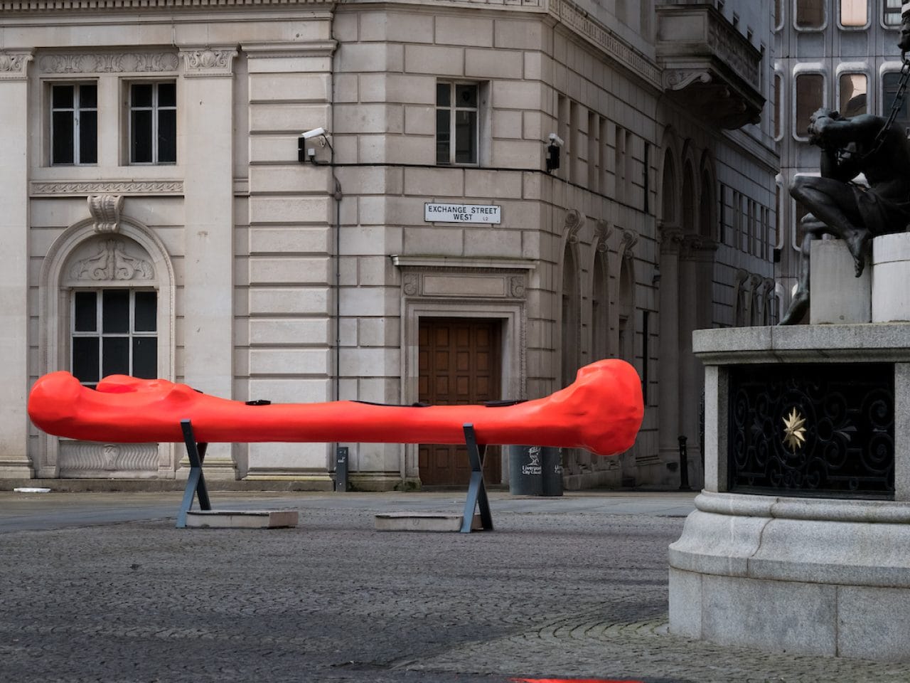 A installation within Exchange Flags, there is a bone shaped canoe, it is bright red and sat on a metal stand.