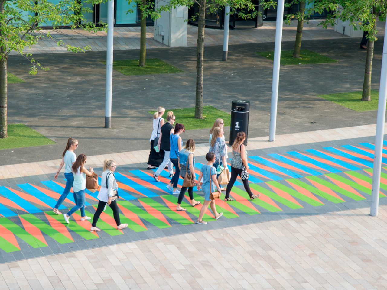 A group of 11 people walking along a blue, green and orange pathway in the city.