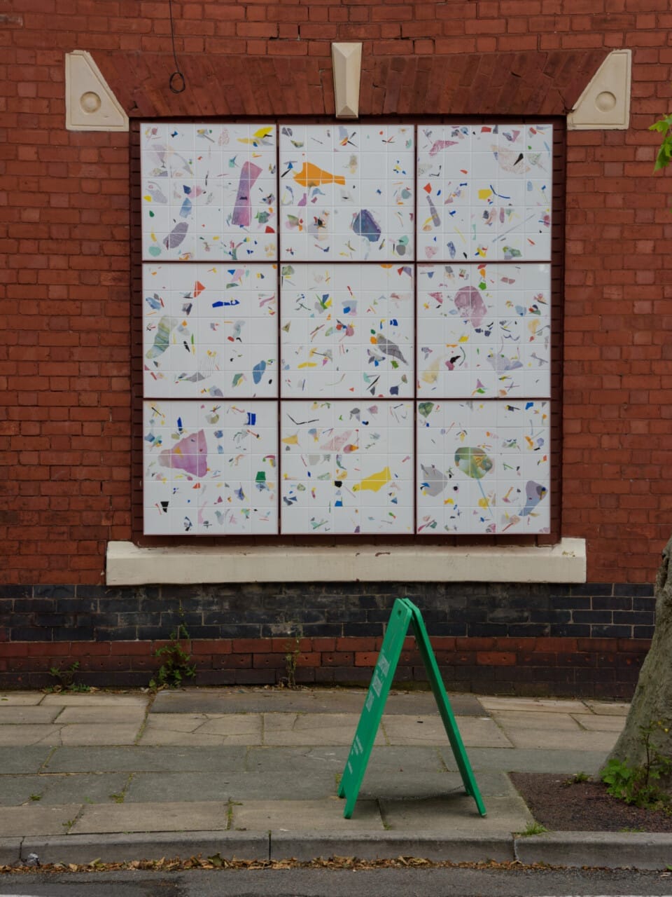 An artwork in a window space with nine white squares with various ceramic embedded pieces.