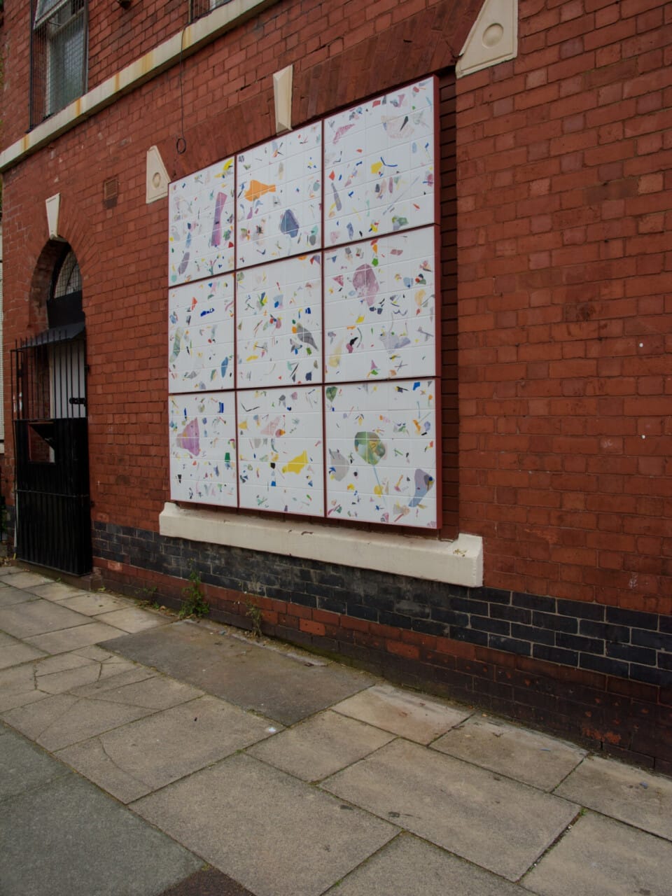 An artwork in a window space with nine white squares with various ceramic embedded pieces.