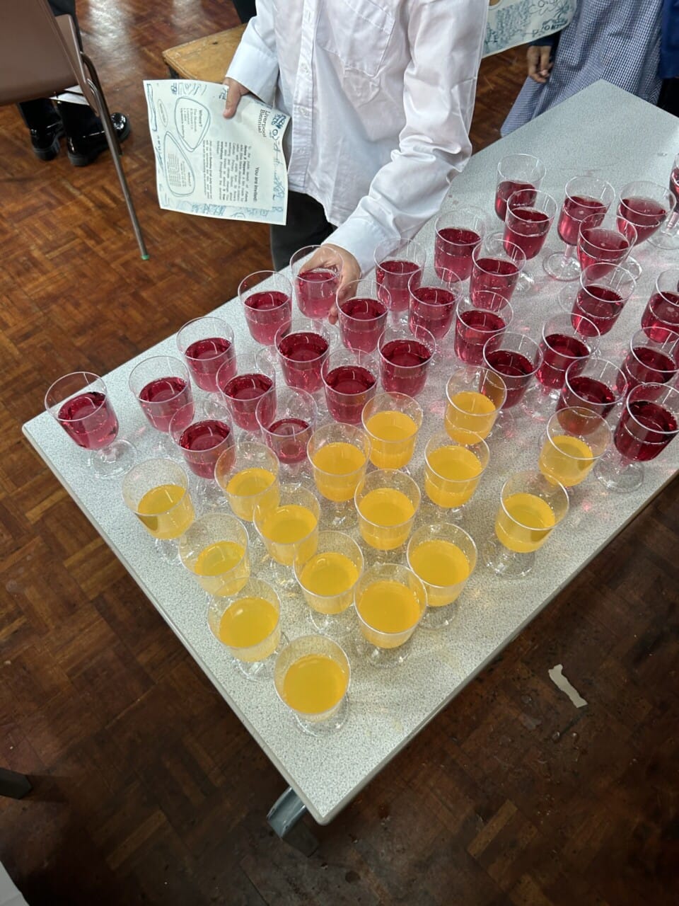 A child picking up a plastic glass from a table of fizzy orange and blackcurrant juice