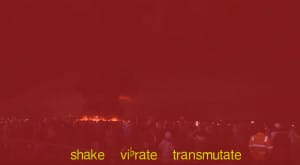 A film still of a red tinted scene of crowds of people with a fire in the distance. At the bottom of the still, it reads 'shake, vibrate, transmutate', in yellow text