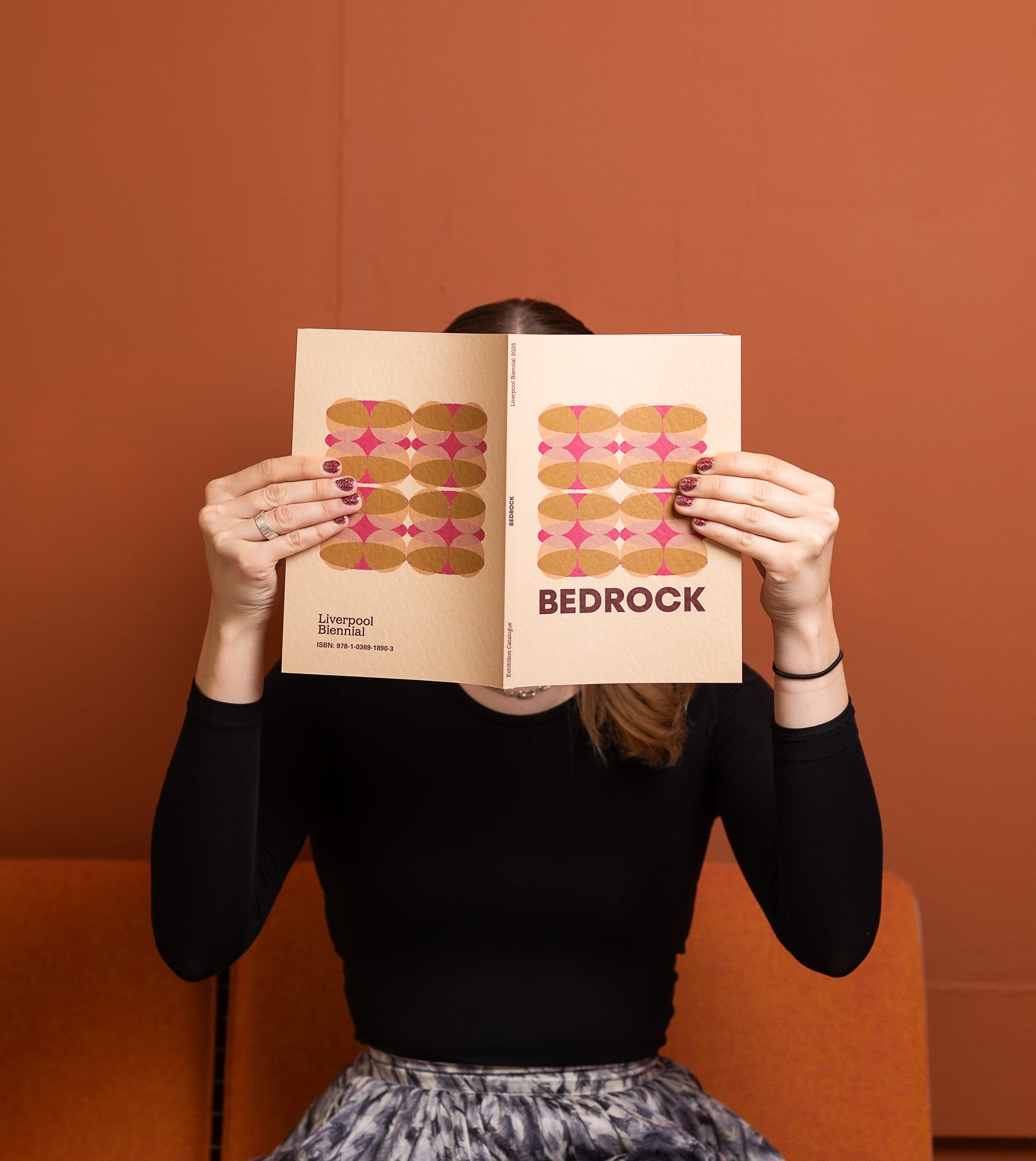 A person holding the pale orange book titled 'BEDROCK' which features colourful shapes on the cover.