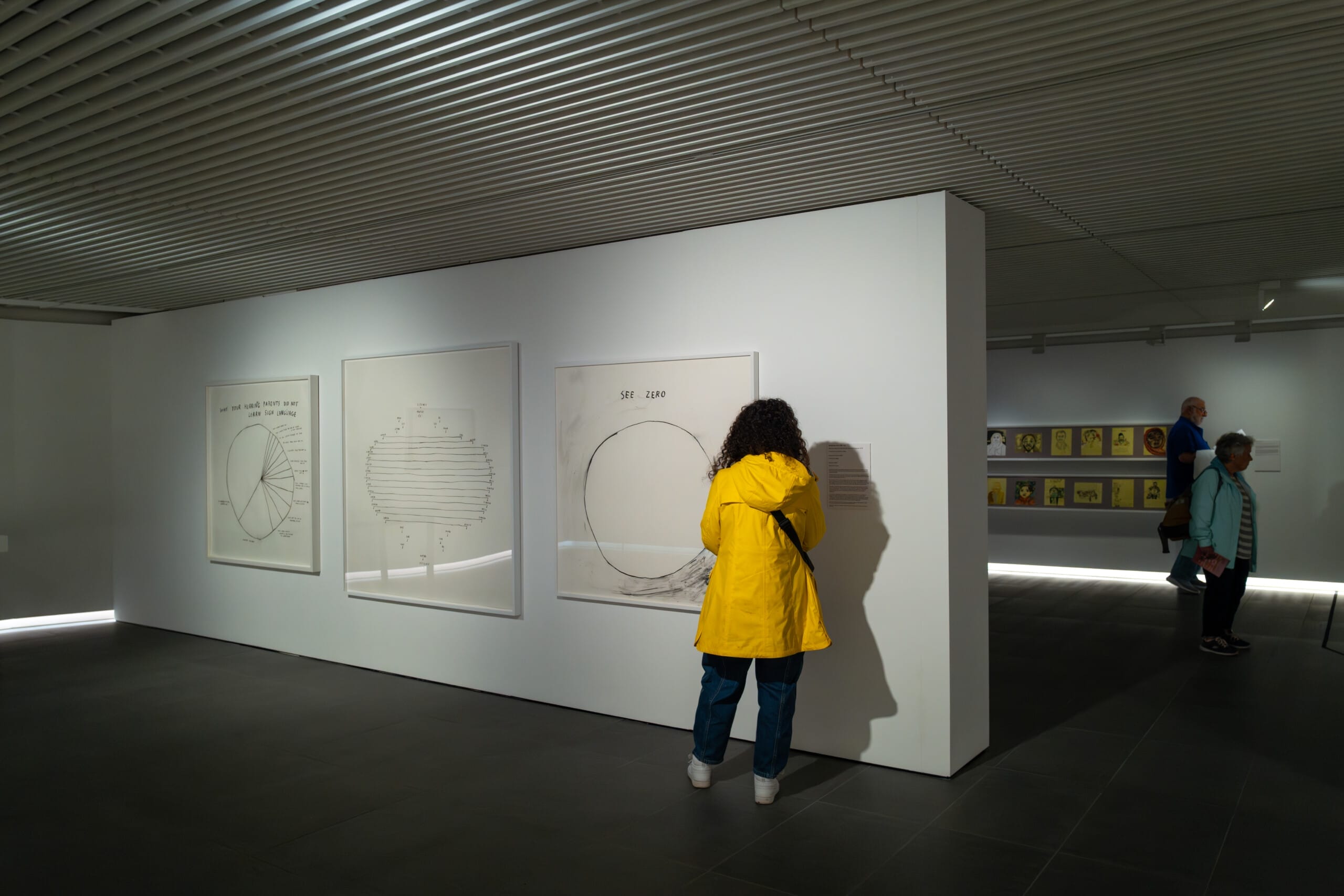 someone standing in a white gallery space, in front of a black and white linear charcoal artwork